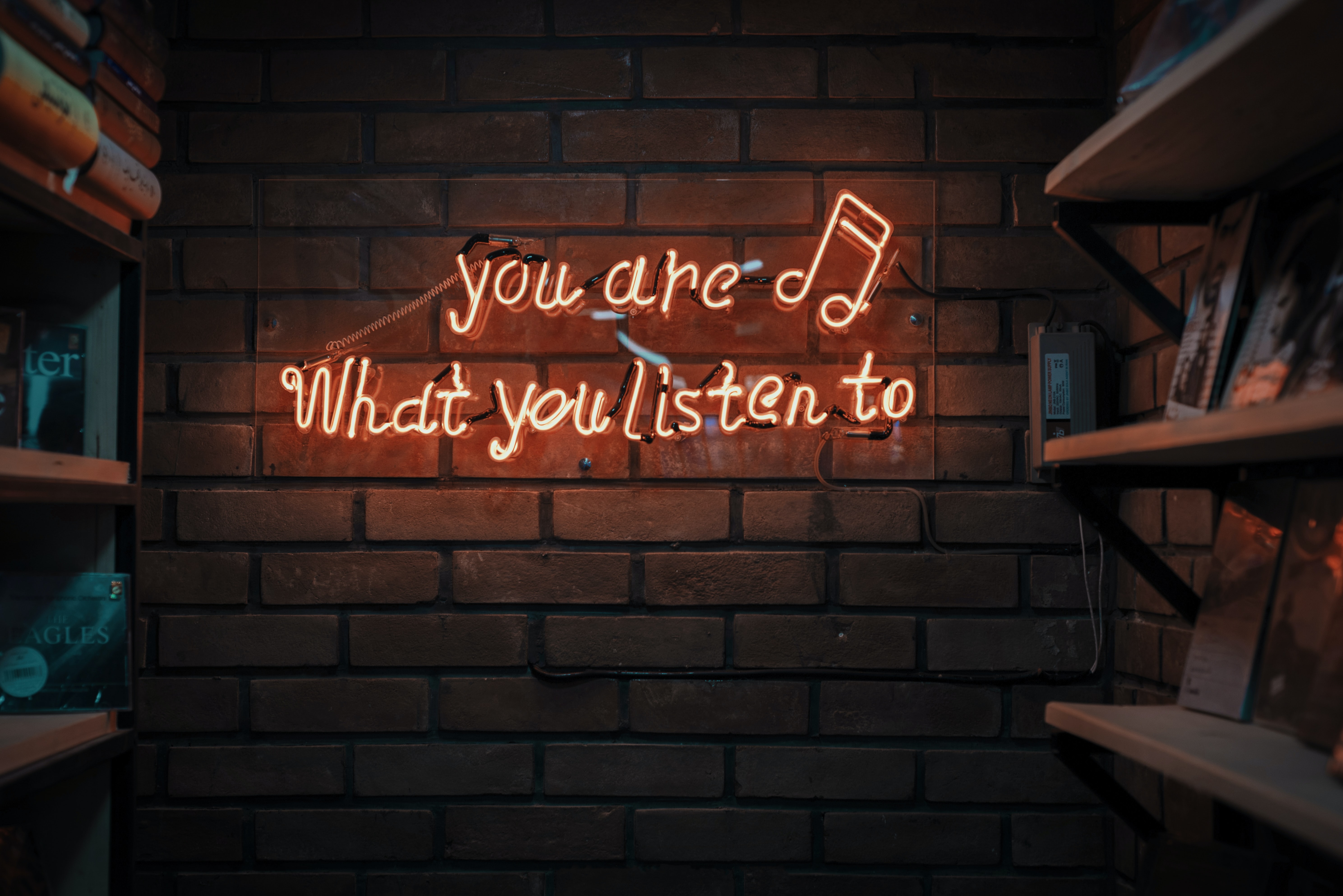 A brick background has a neon sign with the words, 'You are what you listen to'.